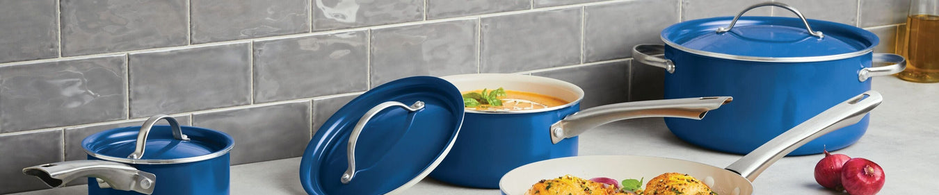 A set of blue cookware, including pots and a pan, is displayed on a kitchen counter with a tiled backsplash. Some lids are off, revealing food inside.