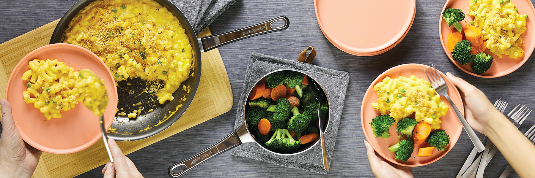 Hands serving pasta with broccoli and carrots from a pan onto plates.