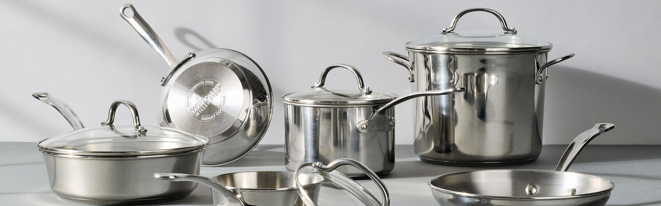 Cookware including saucepans, a pot on a stove, and a pan with pork chops sit on a kitchen counter. A plate with mashed potatoes, green beans, and a pork chop is in front.
