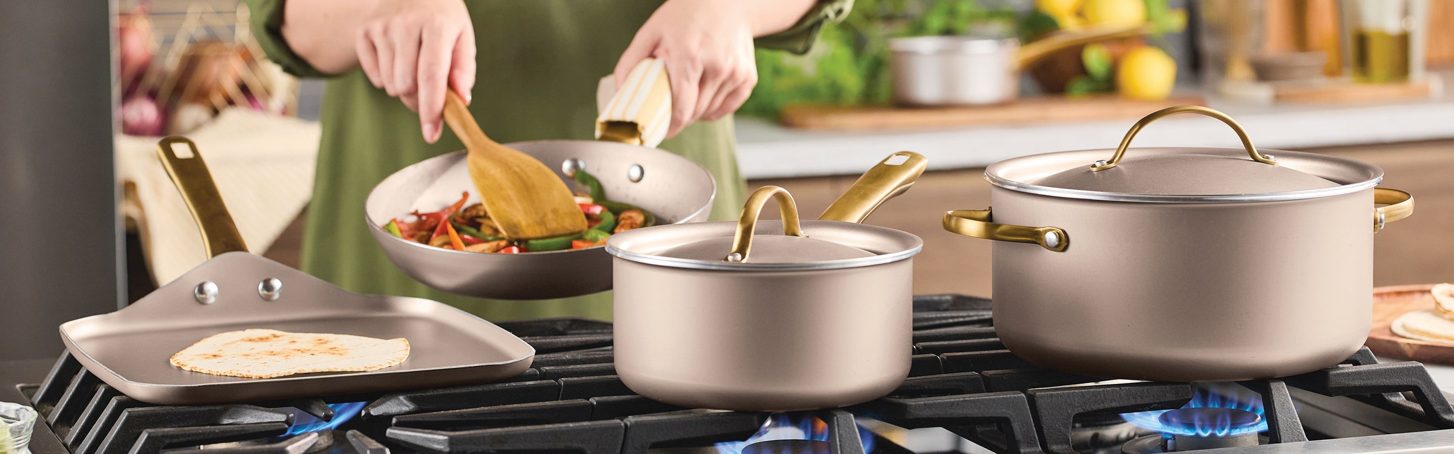 Person cooking vegetables in a frying pan, with a saucepan, griddle with tortilla, and stockpot on a gas stove in a kitchen setting.