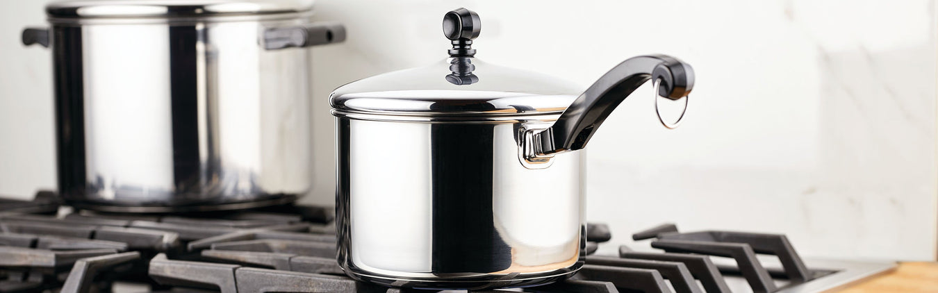 A stainless steel saucepan with a lid and black handle sits on a gas stove, with a larger pot in the background.