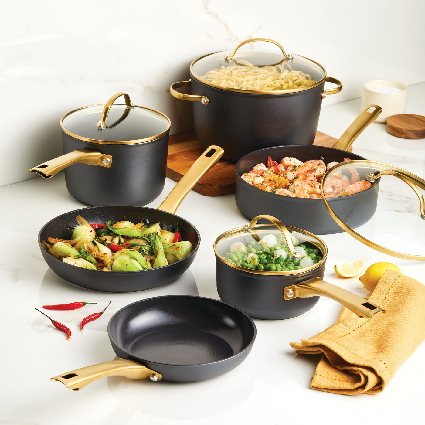 Forged Induction Ceramic 12-Piece Cookware Set in black and gold, crafted from elegant forged aluminum, with vegetables and seafood on a marble surface.