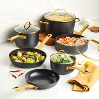 Forged Induction Ceramic 12-Piece Cookware Set in black and gold, crafted from elegant forged aluminum, with vegetables and seafood on a marble surface.