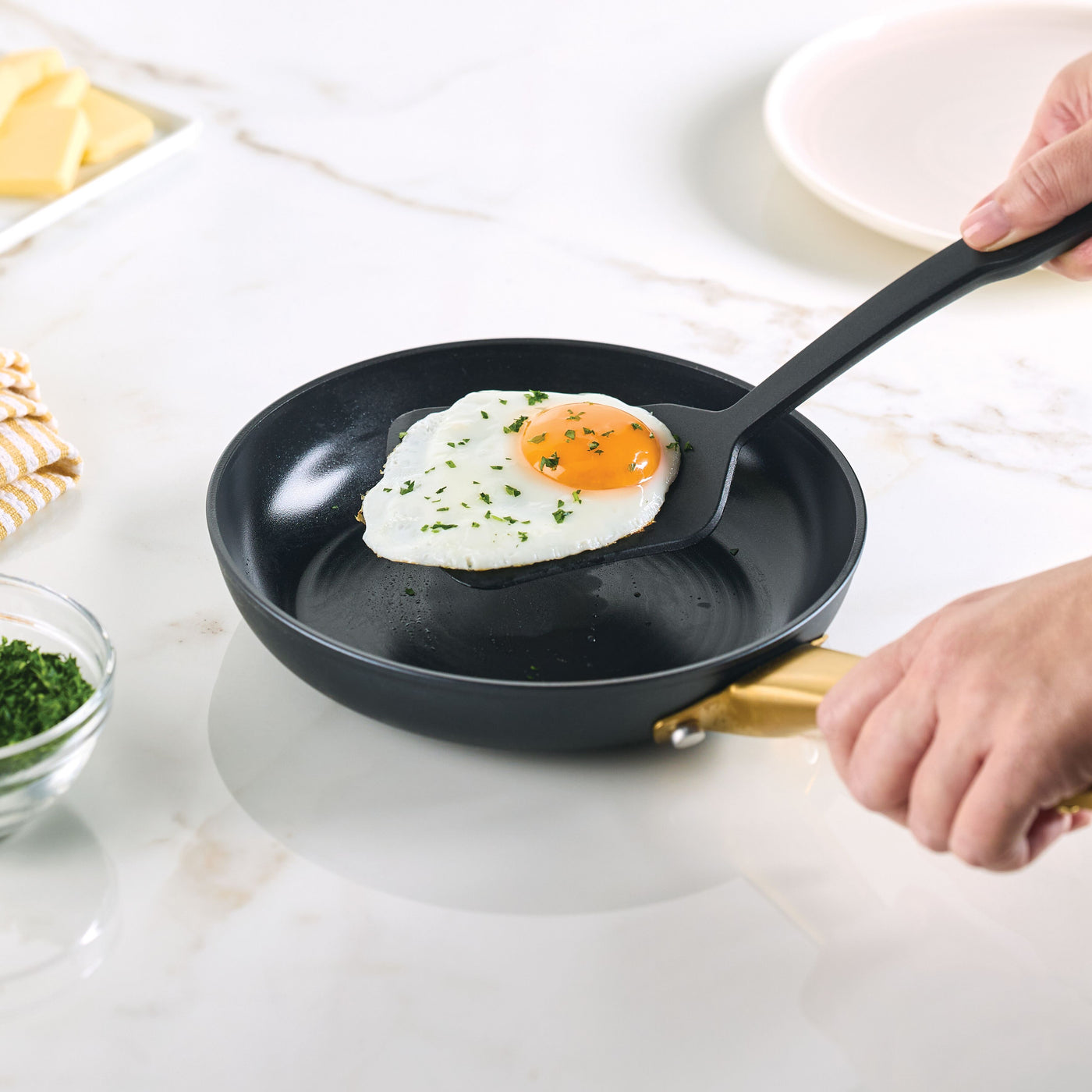A person is frying an egg in a Forged Induction Ceramic 8.25-Inch Frying Pan using a black spatula.