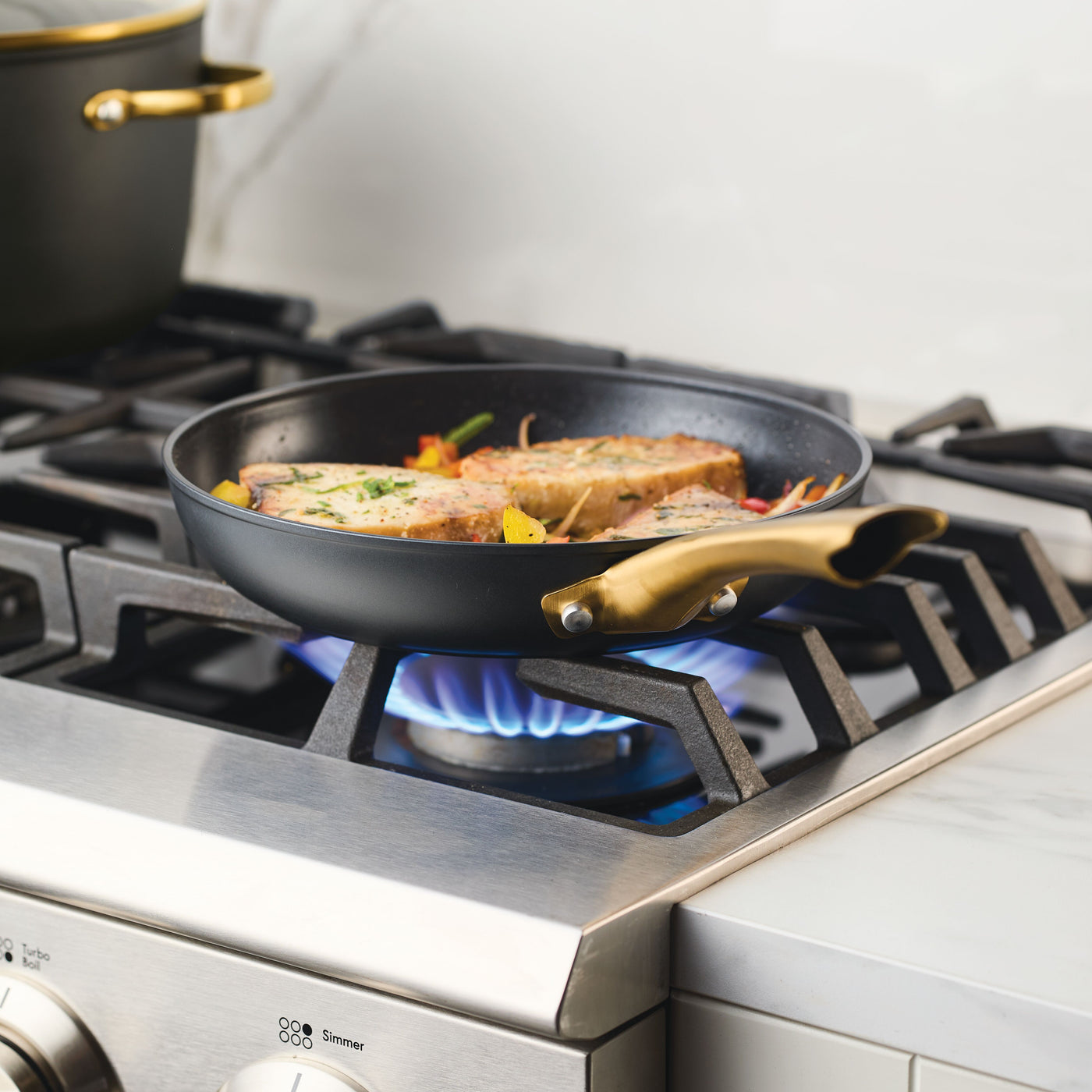 The Forged Induction Ceramic 10-Inch Frying Pan is shown on a lit gas stove burner with food, highlighting its induction-ready ceramic nonstick surface and forged aluminum construction for even heat distribution.