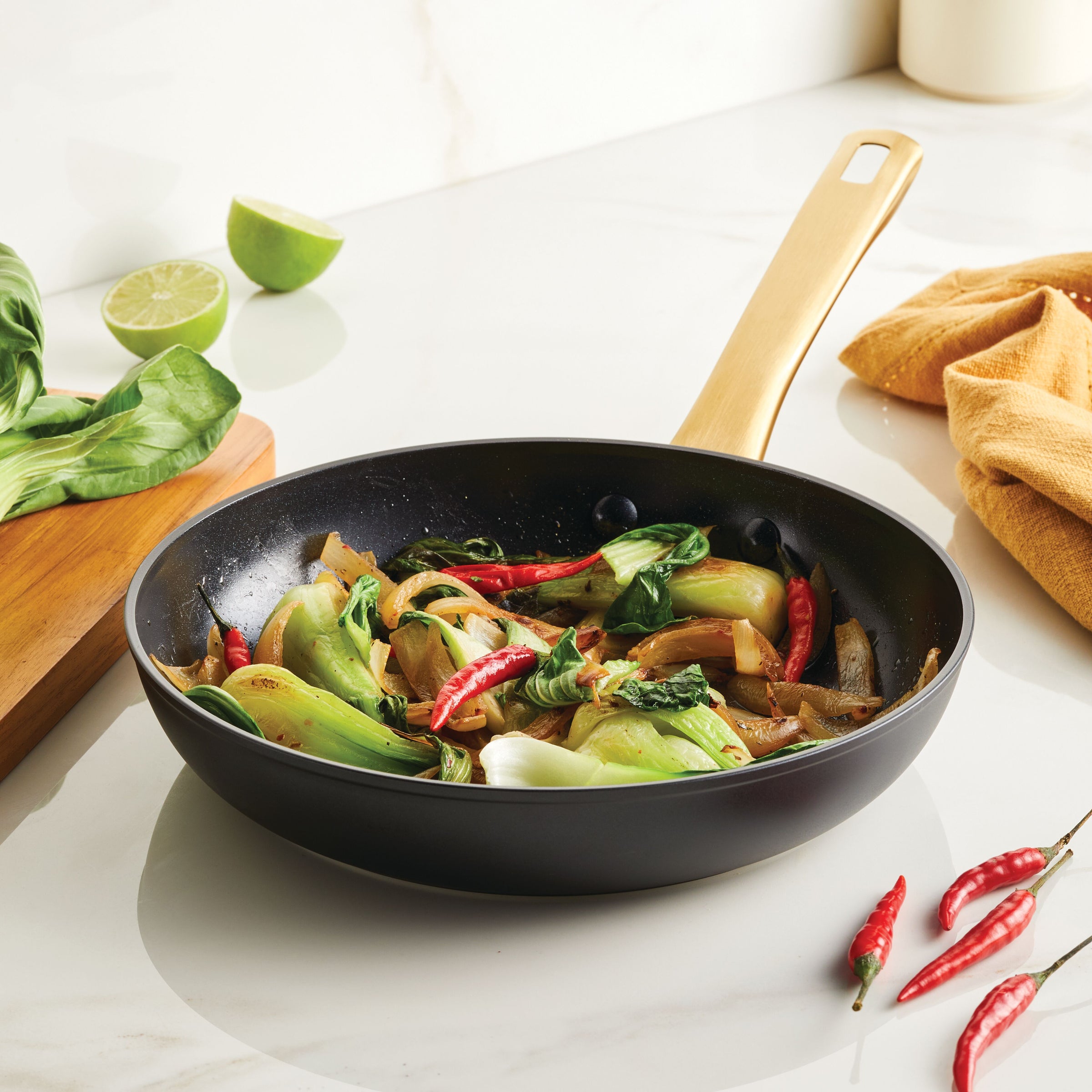 Stir-fried vegetables and chilies sizzle in a Forged Induction Ceramic 10-Inch Frying Pan on a marble surface.