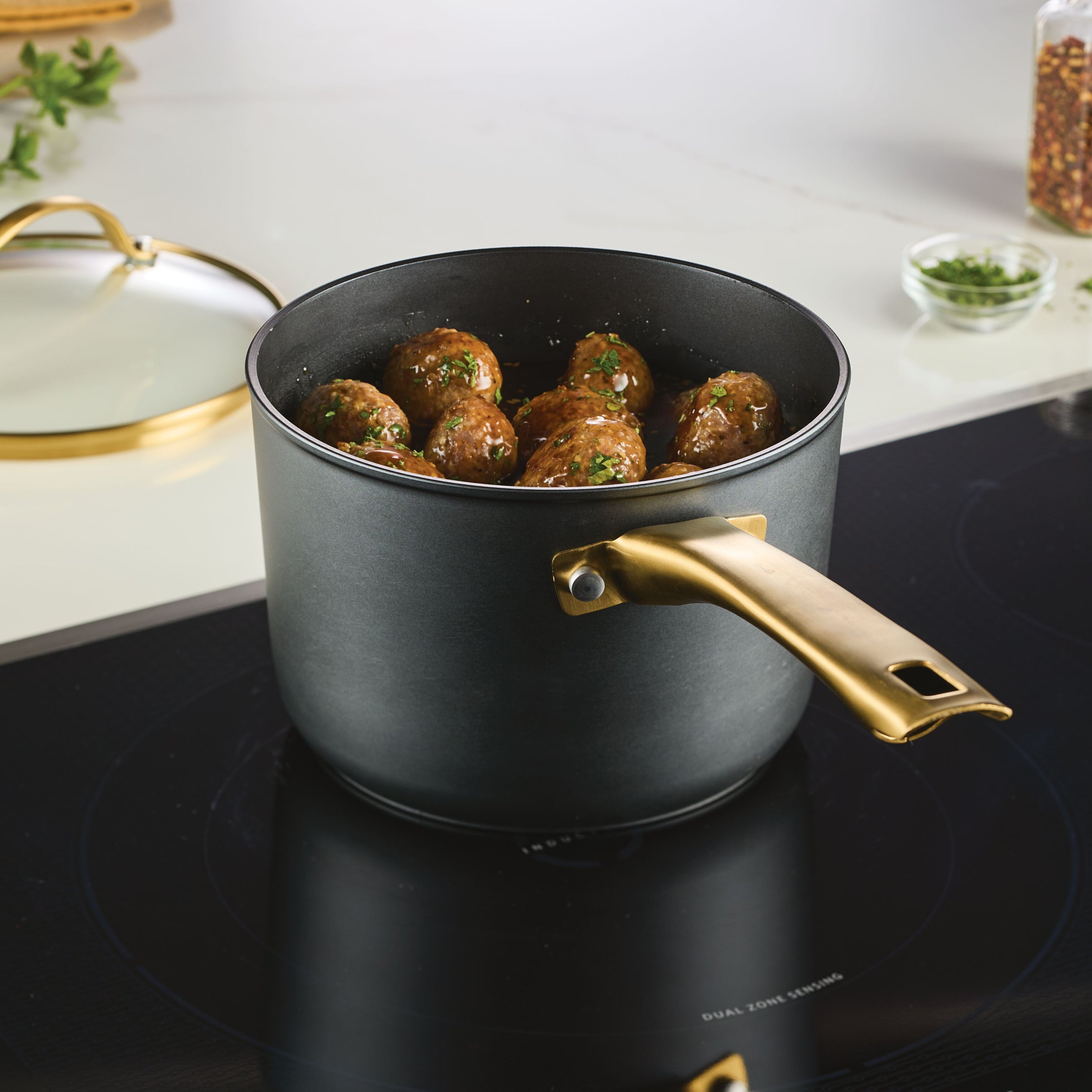 The Forged Induction Ceramic 3-Quart Sauce Pan With Lid gently simmers meatballs on the stovetop, enveloped by aromatic herbs and spices. Its induction-ready ceramic nonstick surface guarantees even cooking, while the forged aluminum construction provides both durability and elegance.