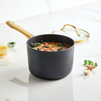 The Forged Induction Ceramic 3-Quart Sauce Pan with Lid, filled with soup and accompanied by garlic and herbs, rests on a marble countertop. It is crafted from forged aluminum and features an induction-ready ceramic nonstick surface.