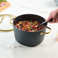 A person stirs a pot of hearty vegetable stew on a marble countertop, using the Forged Induction Ceramic 6-Quart Stockpot With Lid, which ensures even heating and efficiency.