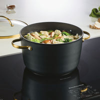 A Forged Induction Ceramic 6-Quart Stockpot With Lid rests on the stovetop, brimming with hearty dumpling soup and fresh vegetables. This induction-ready cookware, crafted from forged aluminum, boasts a ceramic nonstick surface for hassle-free cooking and cleanup.