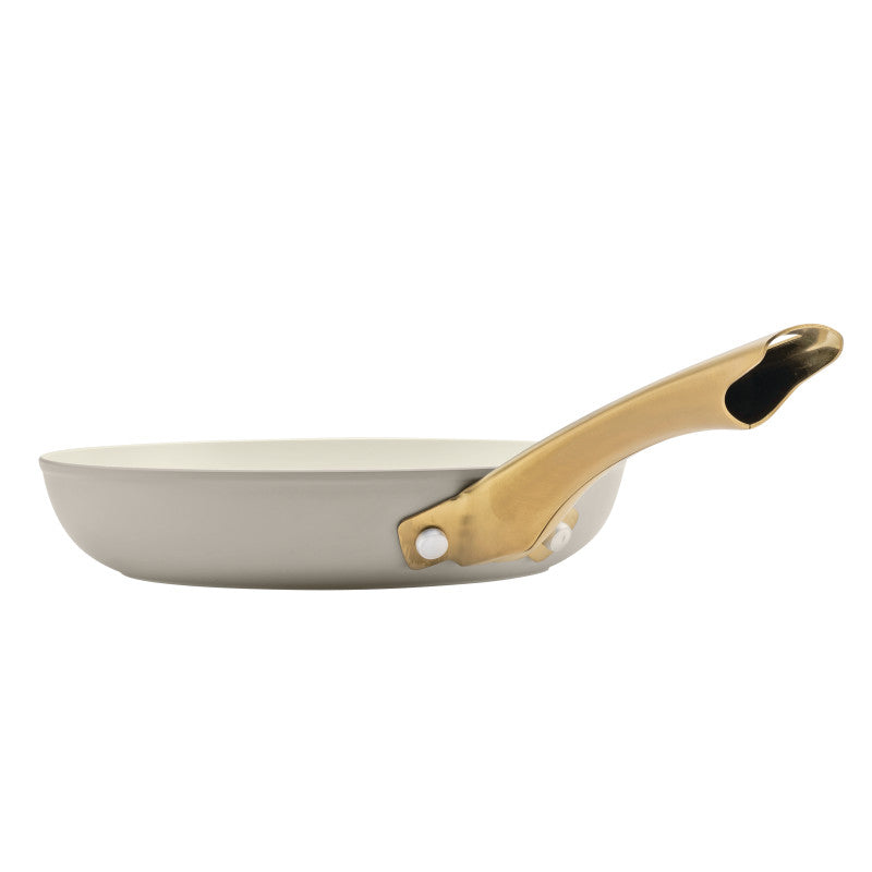 A side-profile view of a Forged Induction Frying Pan in a taupe finish. The pan features a high-performance nonstick interior and a signature gold-tone handle secured with a polished rivet. The handle's hollow-center design and tapered shape are visible against the white background.