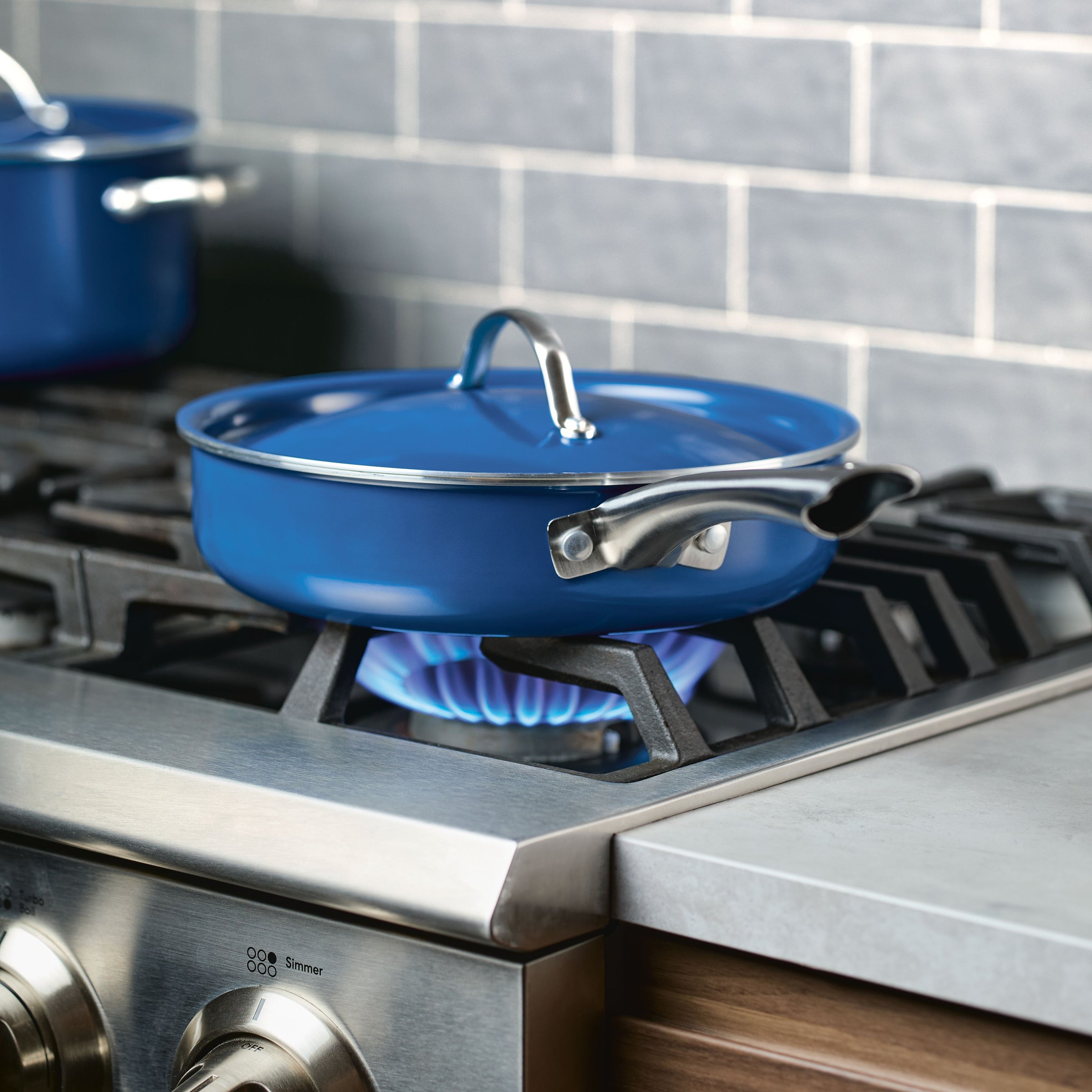 A 2.75 Quart Ceramic Nonstick Saute Pan with Lid, celebrated for its durable cookware quality, sits on a gas stove with a lit burner, seamlessly combining functionality with modern elegant design.