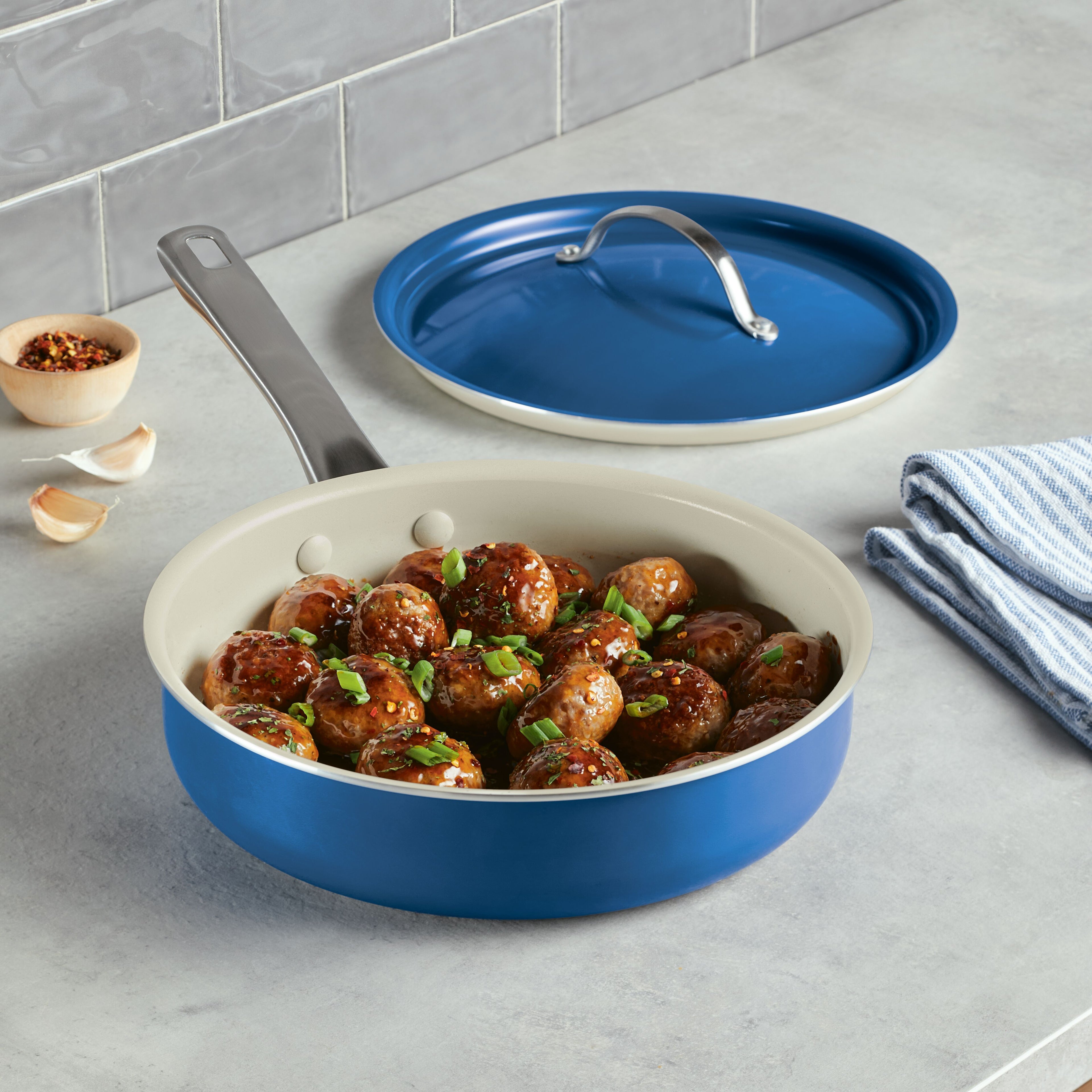 The 2.75 Quart Ceramic Nonstick Saute Pan is showcased with meatballs garnished with green herbs, highlighting its durable design. Next to it are the included lid and a towel, both reflecting a modern and elegant style.