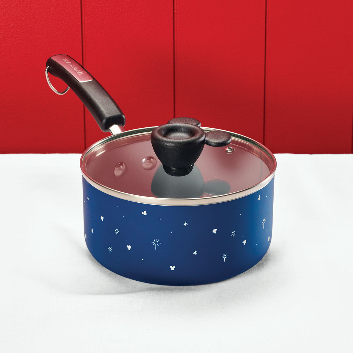 Blue saucepan with a glass lid on a white surface, red wall background.