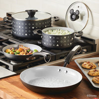 The stove is adorned with Disney-themed cookware, showcasing the 7-Piece Monochrome Ceramic Nonstick Cookware Set from the Mickey Mouse collection. Delicious food sizzles in these ceramic nonstick pans while cookies bake to perfection on the tray.