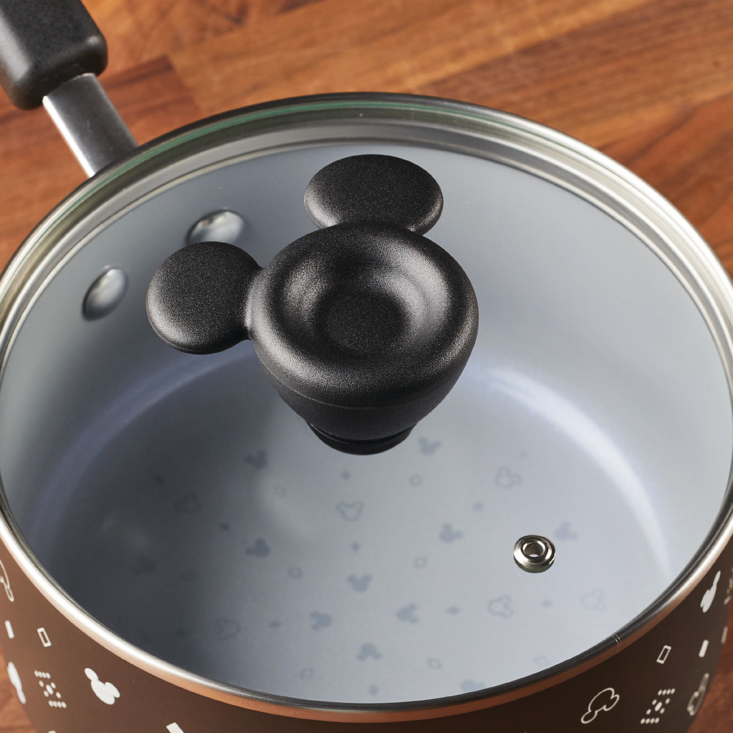 Part of the exclusive Monochrome Collection, the 2-Quart Monochrome Ceramic Nonstick Saucepan with Lid is adorned with a whimsical mouse-shaped handle, bringing charm to your kitchen. Positioned on a sleek wooden surface, it caters to Farberware cookware enthusiasts looking for both functionality and style.
