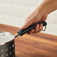 A hand holds a 2-Quart Monochrome Ceramic Nonstick Saucepan with Lid, featuring a Mickey Mouse theme, seamlessly resting on a wooden countertop.