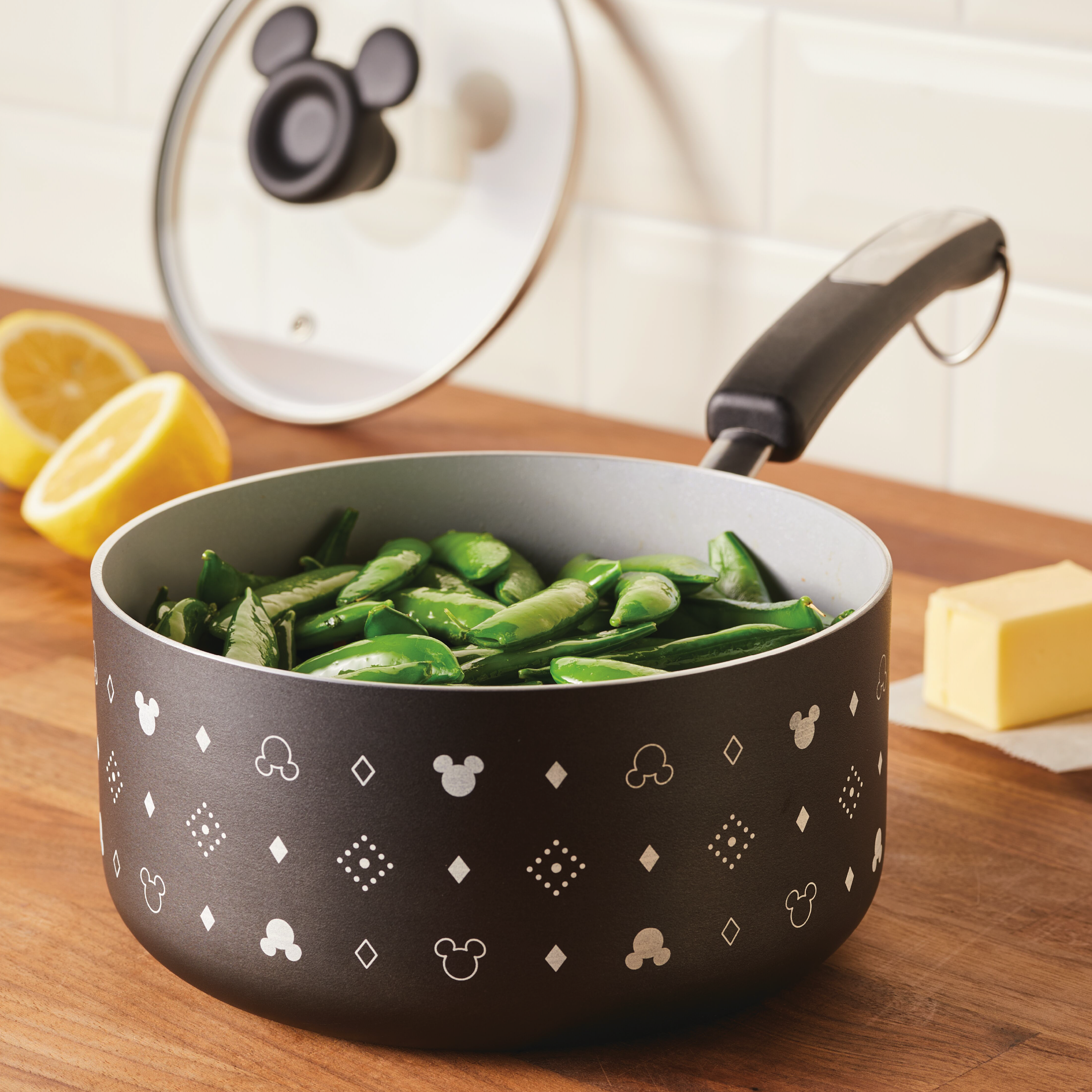 The 2-Quart Monochrome Ceramic Nonstick Saucepan with Lid, distinguished by its black design and decorated with white patterns, is beautifully showcased on a wooden counter filled with vibrant snap peas.