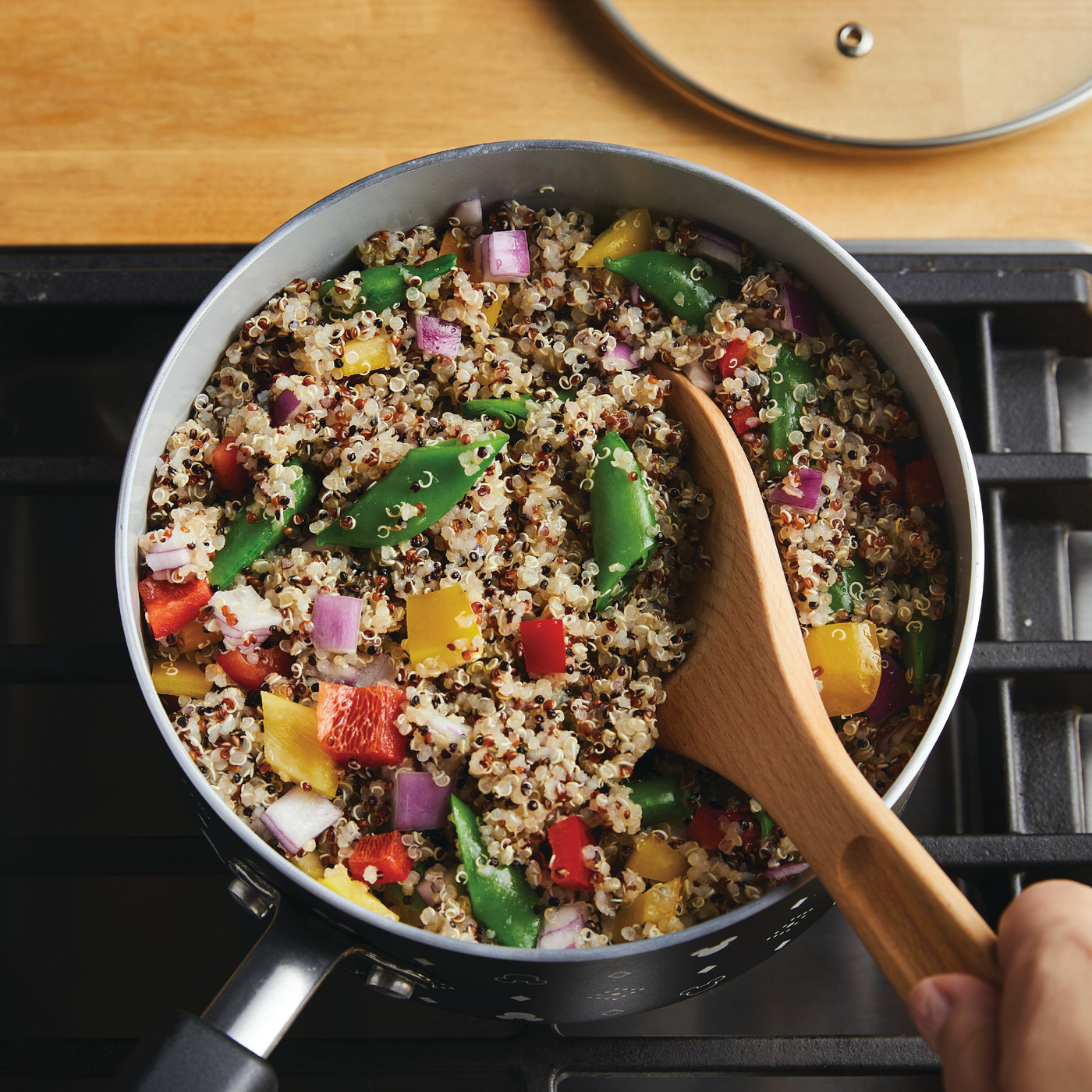 In the Monochrome Collection, a 2-Quart Monochrome Ceramic Nonstick Saucepan with Lid from Farberware cookware sits on the stovetop, filled with quinoa and mixed vegetables, gently stirred with a wooden spoon.