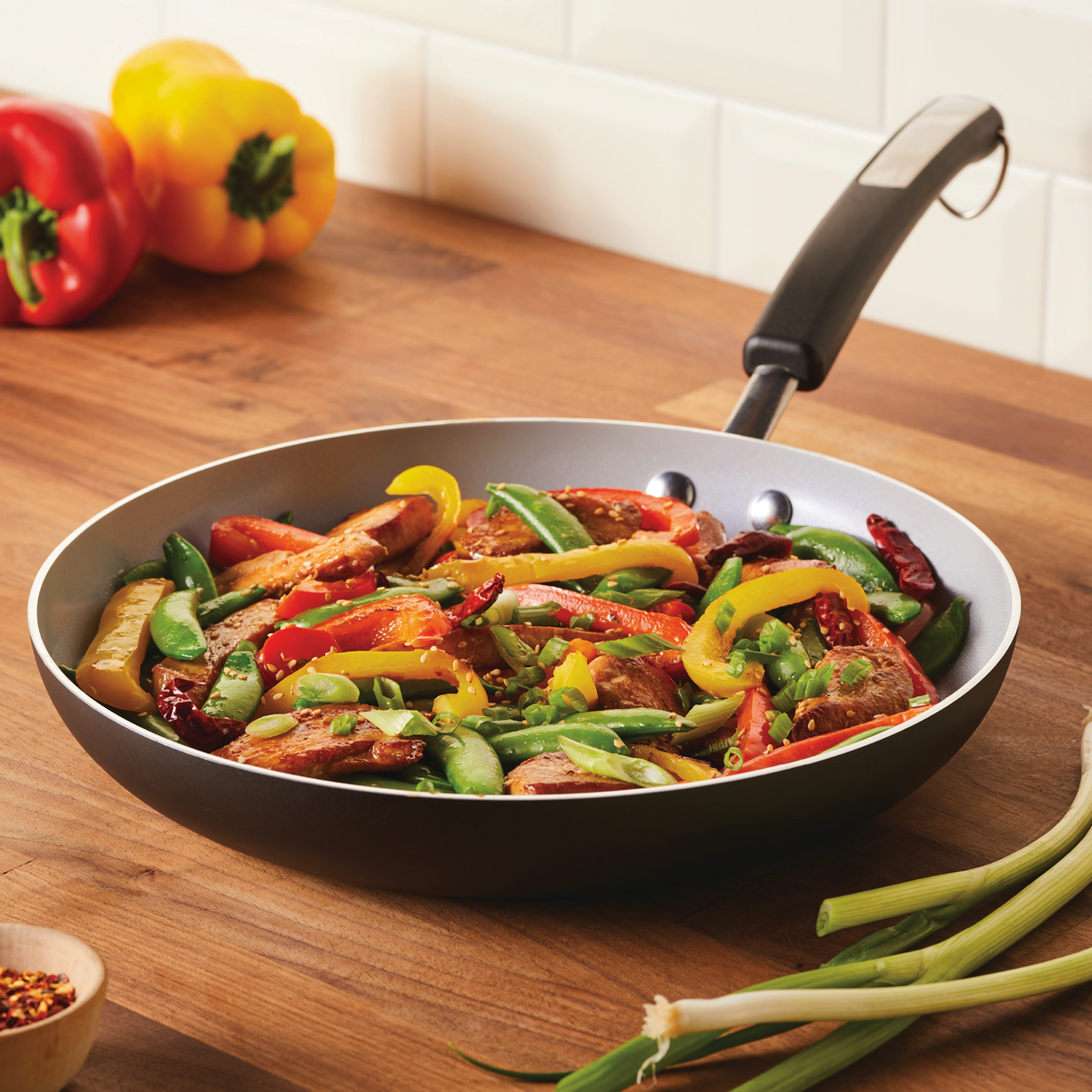 Stir-fry vegetables and chicken in a pan on a wooden kitchen counter.
