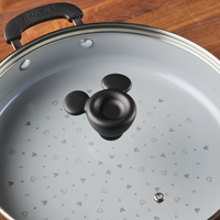 A 4.5-quart Monochrome Ceramic Nonstick Sauté Pan with a lid and helper handle rests on a wooden table, radiating the playful allure of the Mickey Mouse Monochrome Collection.
