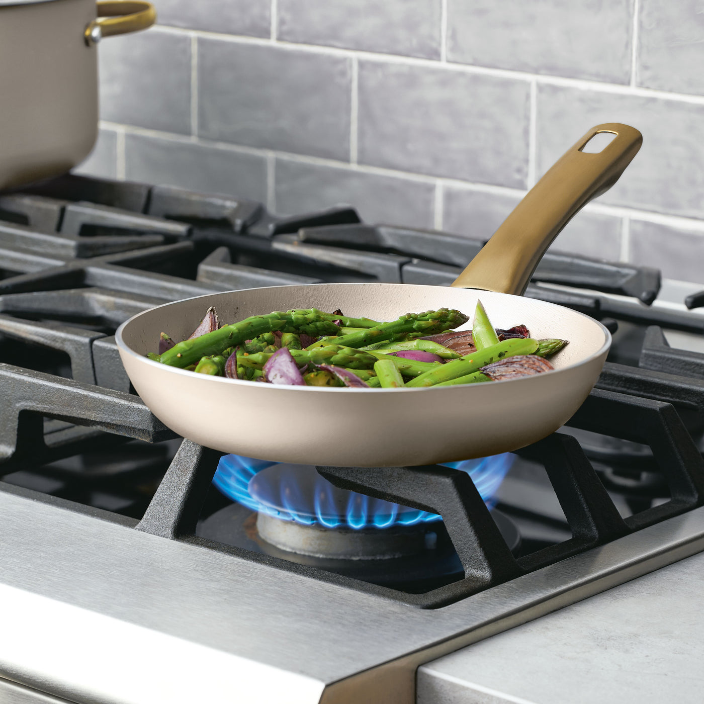 The Radiant Nonstick Frying Pan with its champagne-colored surface is on the stove, evenly heating the asparagus and onions with a blue flame.