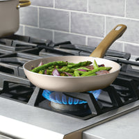 The Radiant Nonstick Frying Pan with its champagne-colored surface is on the stove, evenly heating the asparagus and onions with a blue flame.