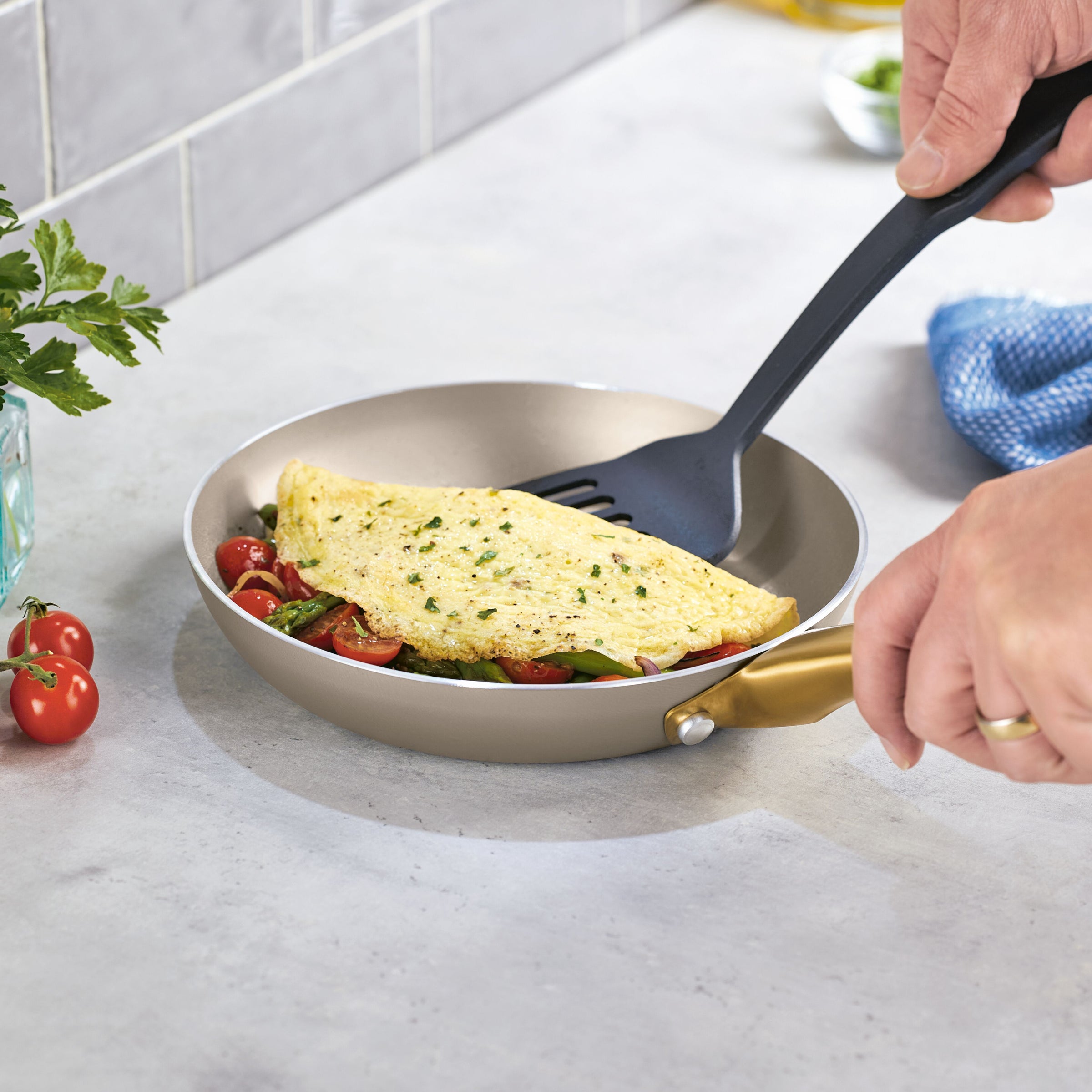 Using the Radiant Nonstick Frying Pan, a person flips an omelette with vegetables, appreciating the even heat distribution across its champagne-colored surface.