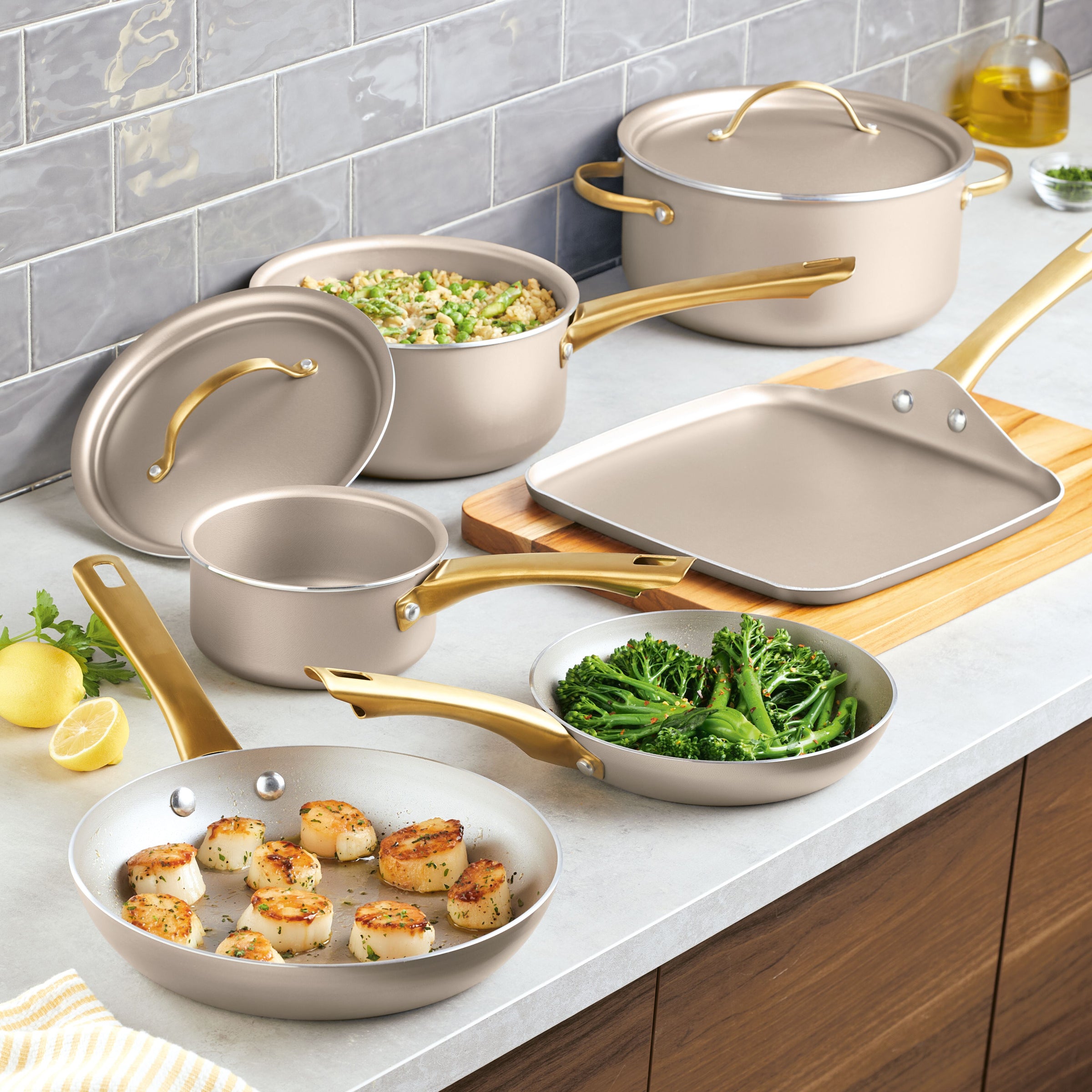 The Radiant Nonstick 12-Piece Cookware Set, featuring pans, pots, and a griddle with gold accent handles, elegantly rests on the kitchen counter.