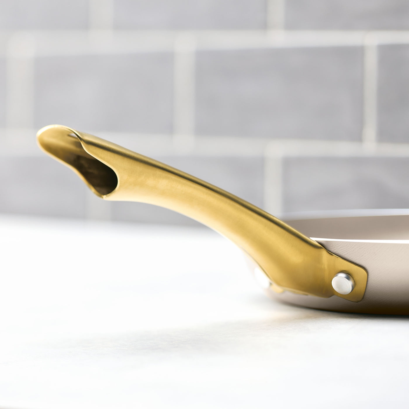 The Radiant Nonstick Frying Pan, featuring a graceful gold handle, is designed with a nonstick surface for consistent heat distribution. Set against a white background, its champagne-colored finish brings an element of sophistication to any kitchen decor.