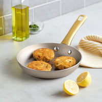 Three crab cakes sizzle in the Radiant Nonstick Frying Pan, accompanied by zesty lemons and a striped towel, ensuring even heat distribution for perfectly cooked results.