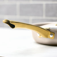 Close-up of a gold accent handle on the Radiant Nonstick 2.75-Quart Saute Pan With Lid, resting elegantly on the stove.