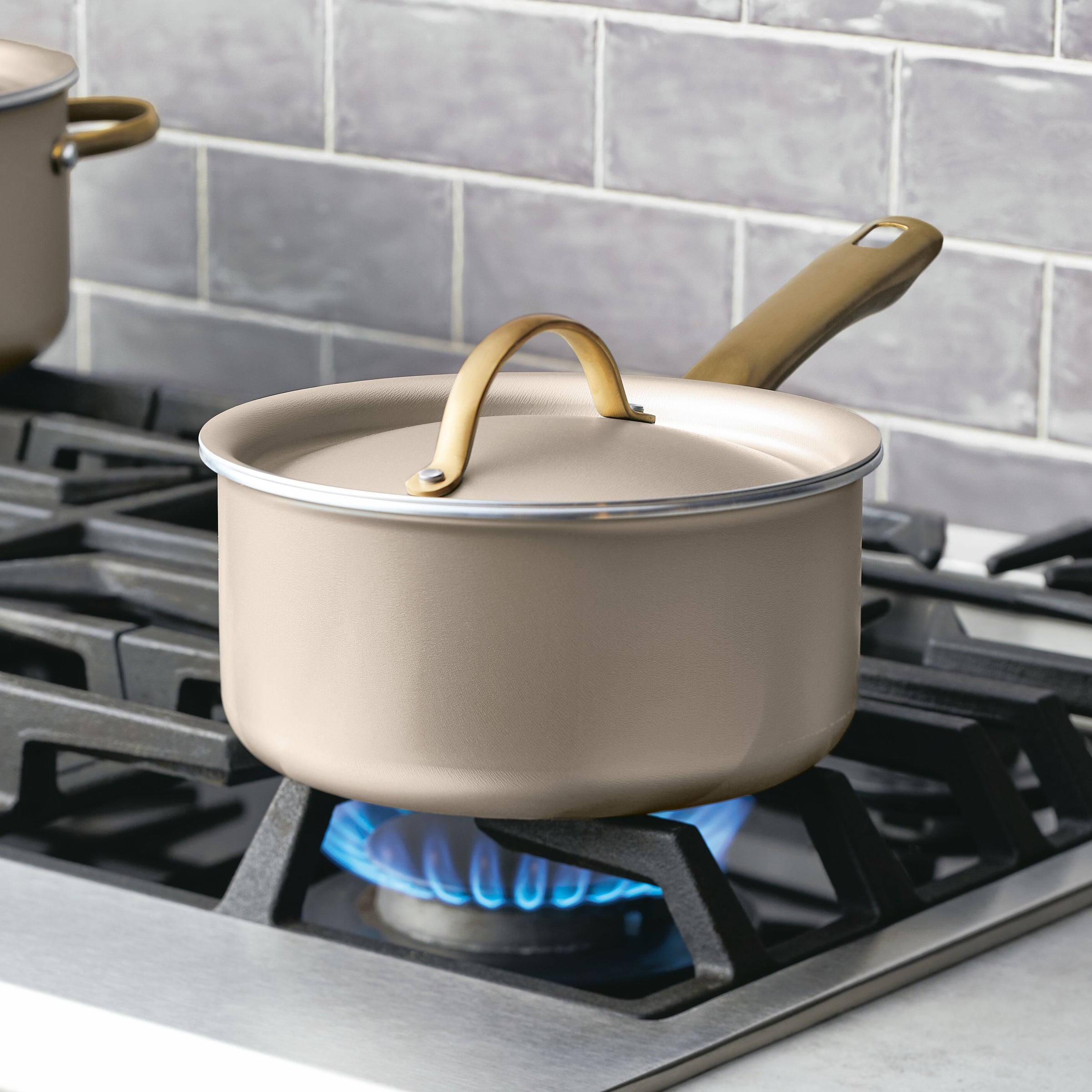 The Nonstick Saucepan with Lid in beige sits on the gas stove's blue flame, ensuring optimal heat distribution.