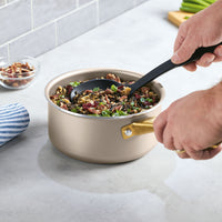 Using the Nonstick Saucepan with Lid, a person expertly stirs rice and vegetables on a kitchen counter, ensuring even heat distribution.
