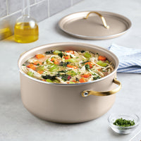 A Radiant Nonstick 5.5-Quart Dutch Oven With Lid brims invitingly with vegetable soup, its exceptional heat distribution ensuring every herb-infused spoonful is perfectly cooked. On the side, a small bowl of garnish promises to elevate each serving.