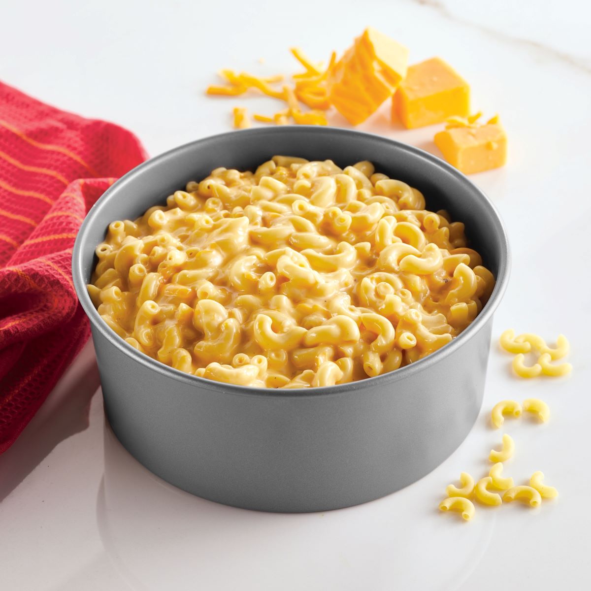 A round pan of creamy macaroni and cheese, made effortlessly in the 4-Piece Nonstick Specialty Bakeware Set by Farberware, with cheese cubes on the side for a delightful finish.