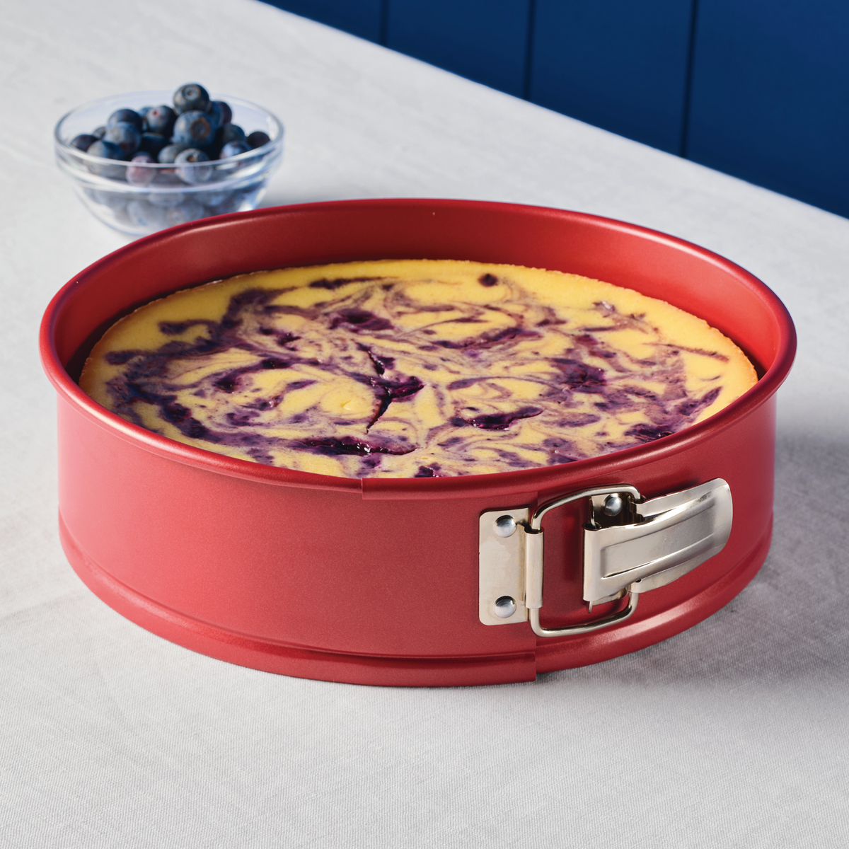 A blueberry swirl cheesecake in a red springform pan on a table.