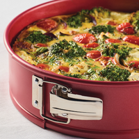 Red baking pan with vegetable quiche topped with broccoli and tomatoes.