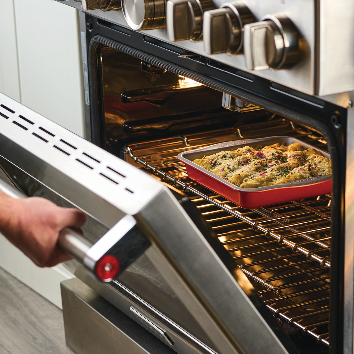 Person placing a casserole dish of food into an open oven.