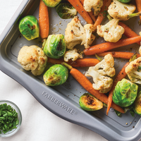 Roasted vegetables on a baking tray next to a small bowl of chopped chives.