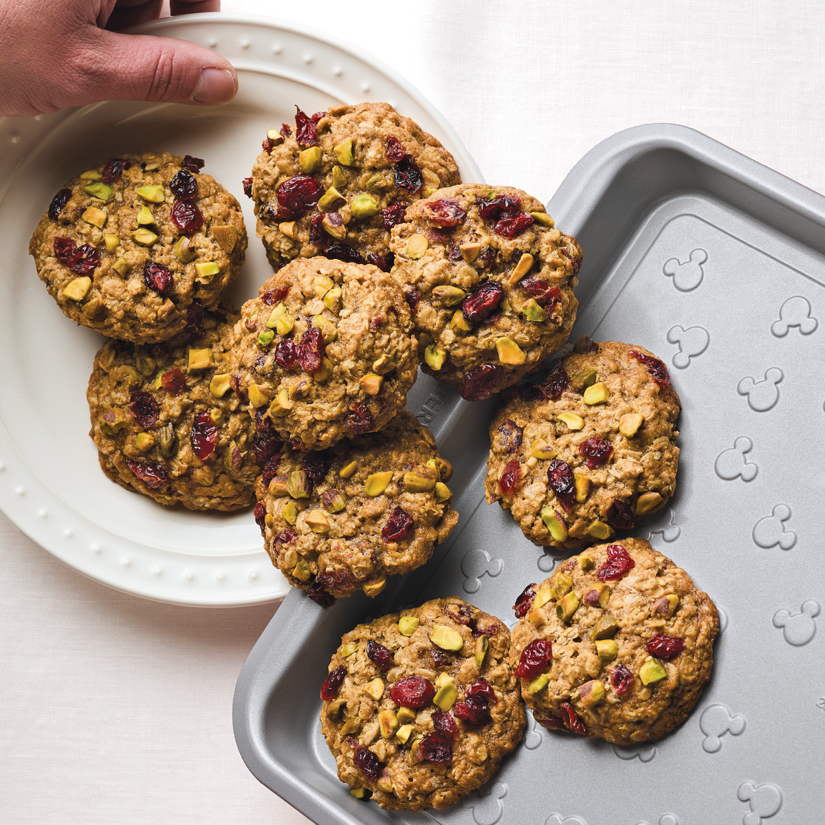 Hand placing cookies with nuts and berries from baking tray onto a plate.