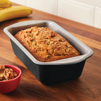 Loaf of banana bread with nuts in a 9"x5" Nonstick Loaf Pan on a wooden counter.