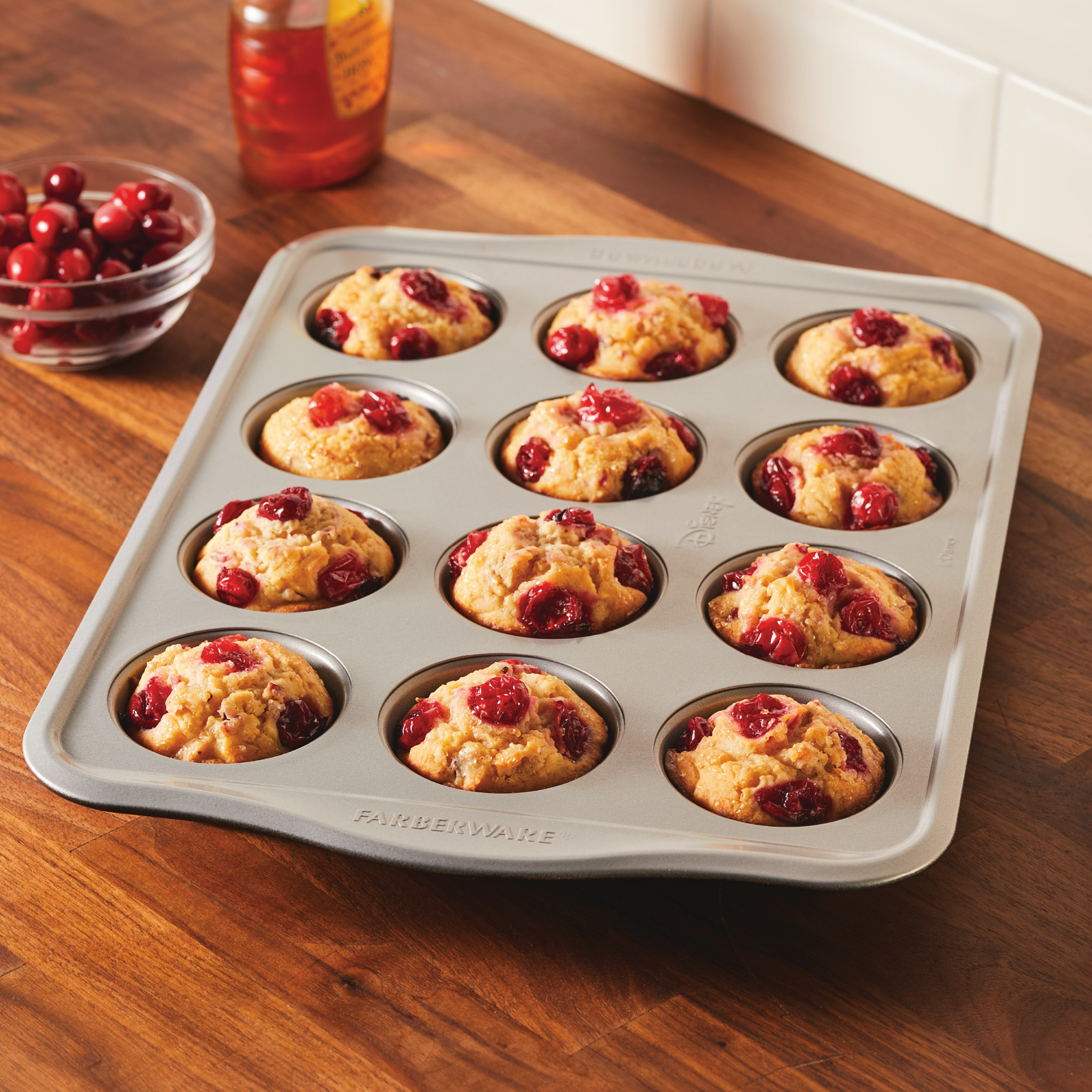 A delightful tray of freshly baked muffins infused with cranberries sits on a wooden table, made perfectly using our innovative 12-Cup Nonstick Muffin Pan from the new bakeware line. Bake with Mickey and experience magic in every bite!