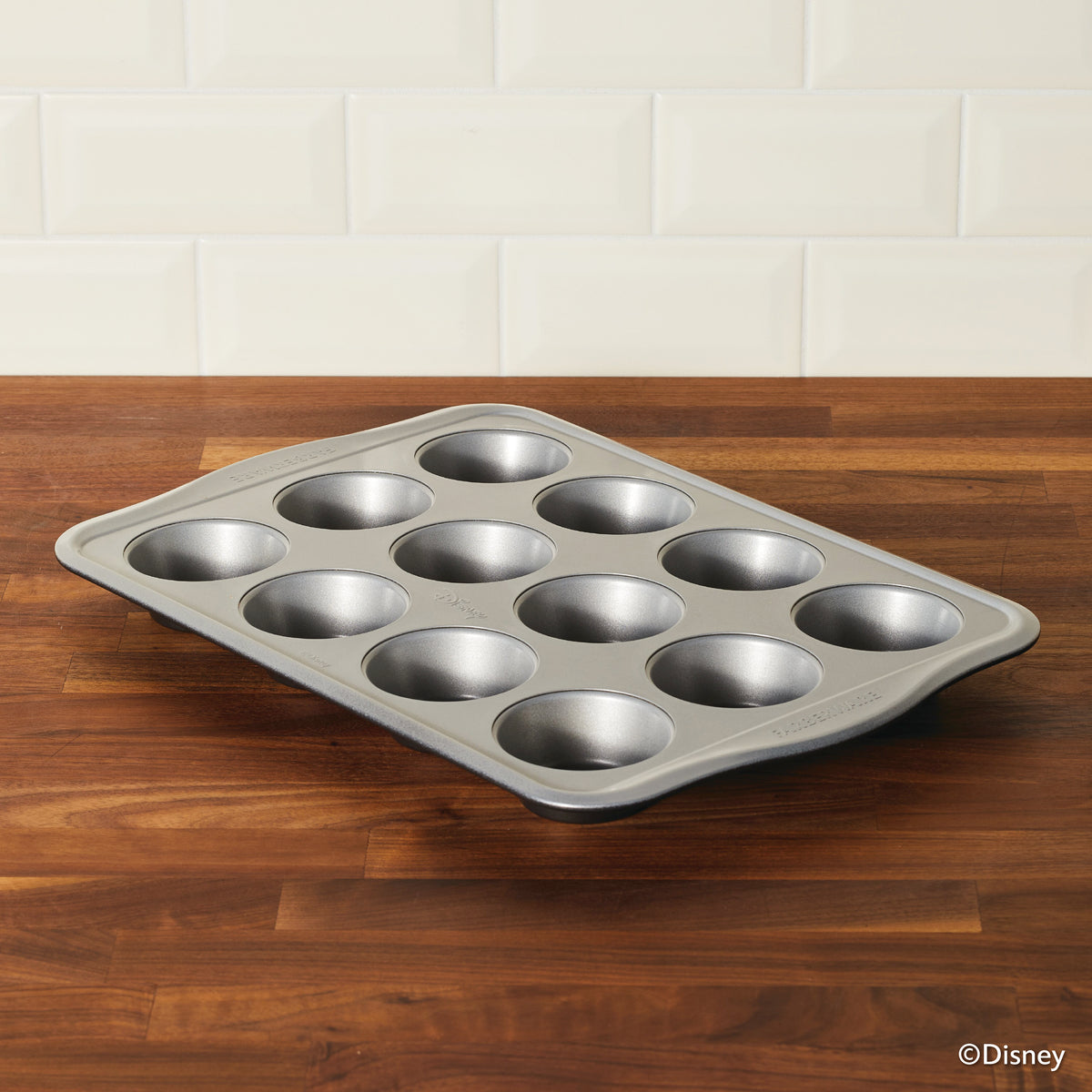 A 12-cup muffin pan on a wooden countertop with a tiled backsplash.
