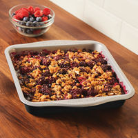 Baking in a nonstick square cake pan on a wooden countertop, bowl of berries behind. Perfect for those who love to bake with Mickey!