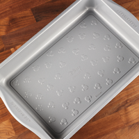Silver baking pan with Mickey Mouse pattern on a wooden surface.