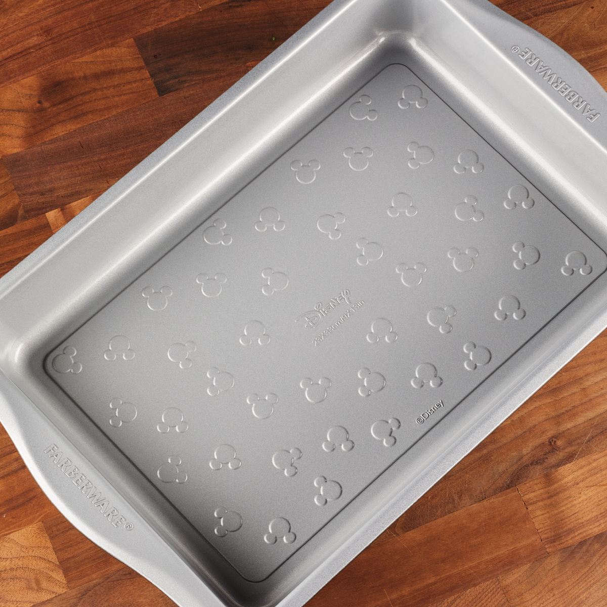 Silver baking pan with Mickey Mouse pattern on a wooden surface.