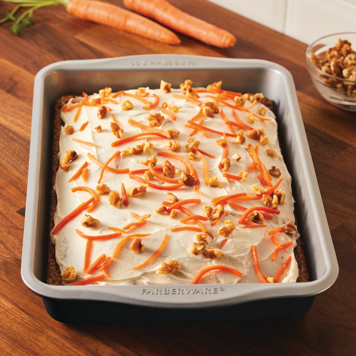 Carrot cake in a baking pan topped with cream cheese frosting and walnuts.