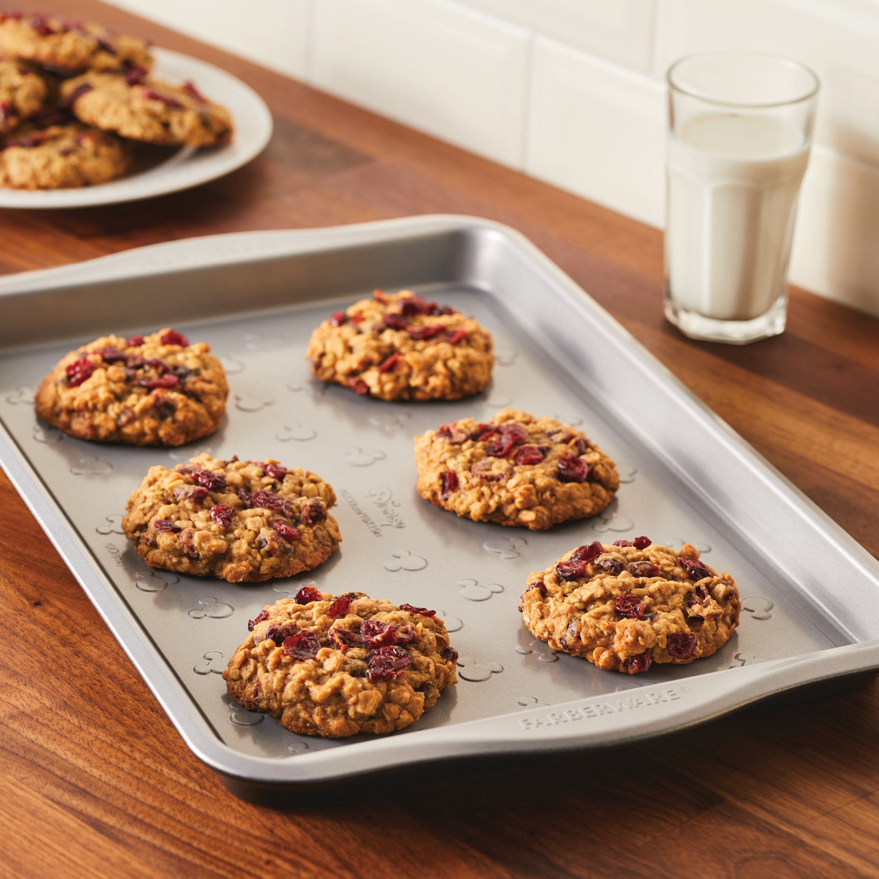 Freshly baked treats on a 10" x 15" Nonstick Cookie Pan, accompanied by a glass of milk in the background, evoke nostalgic warmth.