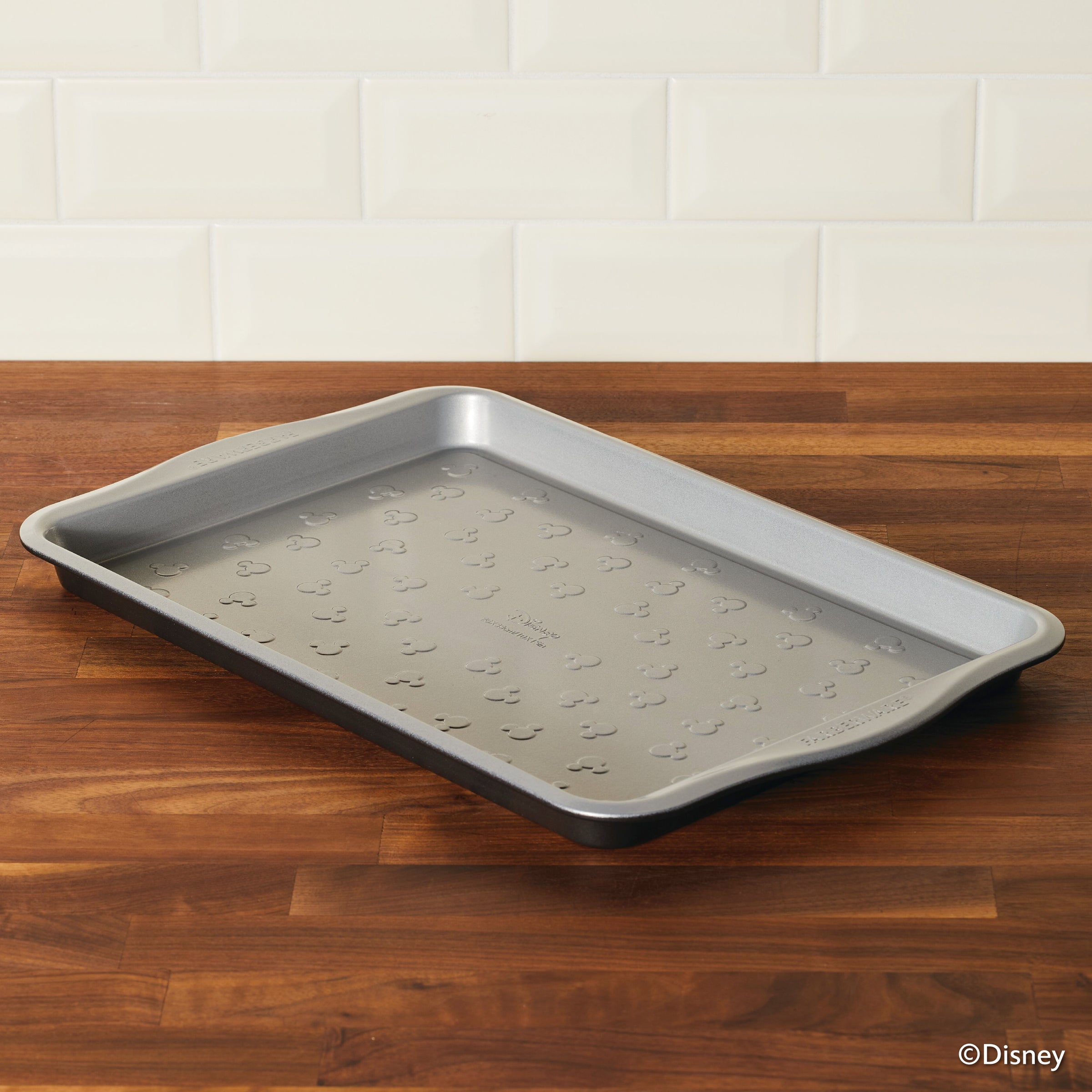 The 10" x 15" Nonstick Cookie Pan sits charmingly on a wooden countertop, featuring a delightful pattern that transforms an ordinary sheet pan into a whimsical kitchen accessory.